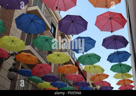 L'abri d'une rue à travers une série d'ouverture de couleur parasols pendu sur les câbles, avec un bleu ciel nuageux, à Orihuela, Espagne Banque D'Images