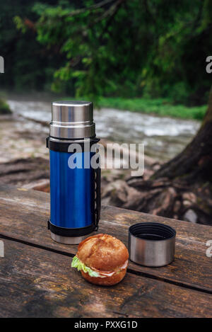 Vue sur le thermos bleu sur la table en bois sur le sentier de randonnée. Pause pour boisson chaude. Banque D'Images