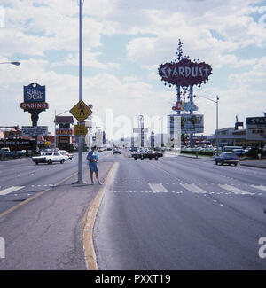 1975, historique, jour et une dame se tient au milieu de la 'bande', un boulevard central dans la ville de casino Las Vegas, Nevada, USA. Un signe de la route (1967) pour le 'Stardust', la célèbre station Hotel and Casino qui a ouvert ses portes en 1958, peut être vu dans la photo et a été formé par un éparpillement des formes graphiques qui éclairés la nuit. Banque D'Images