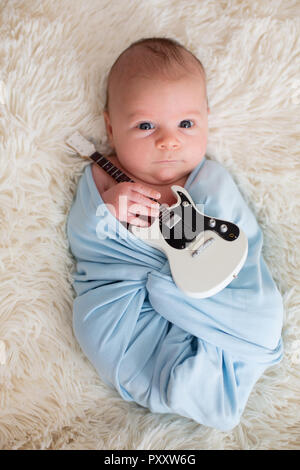 Bébé nouveau-né garçon, enveloppé dans l'écharpe bleue, tenant un peu de guitare et smiling Banque D'Images