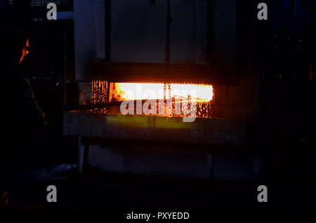 L'ouvrier durcit le métal dans un énorme four chauffé au rouge dans l'atelier de production de l'usine. Pièces forgées lourd rideau d'eau chaude Fiery. Banque D'Images