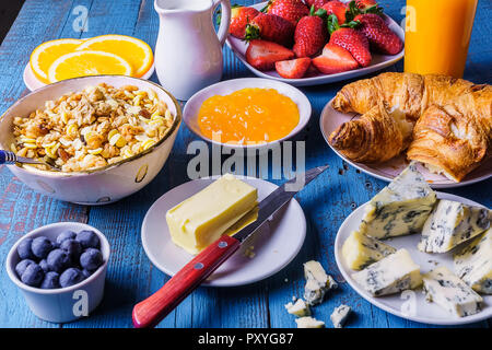 Petit-déjeuner sain avec granola, fraise, fromage, jus, confiture, croissant, le lait dans un petit jur, orange, fruits bleu sur fond de bois. Banque D'Images