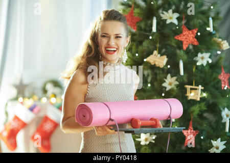 Femme au foyer à la mode sourire avec matériel de remise en forme près de l'arbre de Noël Banque D'Images