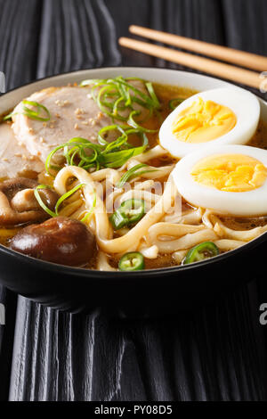 Soupe Asiatique aux nouilles Udon, porc, œufs, oignons et champignons shiitake close-up dans un bol sur la table verticale. Banque D'Images