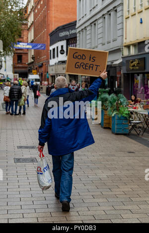 Rue fontaine de Belfast en Irlande du Nord. 24 octobre 2018 Homme marchant à travers Belfast avec "Dieu est Grand" écrit sur un tableau de liège Banque D'Images