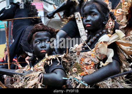 Les enfants avec des traînées noires visages dans des costumes tribaux en face de l'équitation homme Atihan Ati à Kalibo, festival, Aklan, Philippines, l'île de Panay Banque D'Images