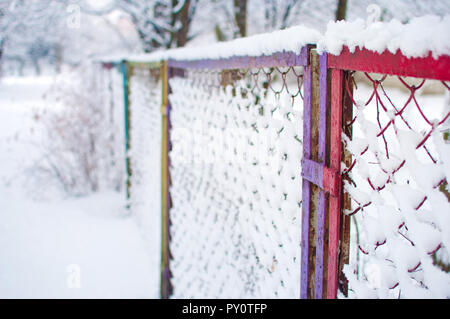 Libre d'un grillage de séparation colorés recouverts d'une épaisse couche de neige duveteux blanc frais contre les arbres et arbustes floue sur l'arrière-plan. D'hiver froid Banque D'Images