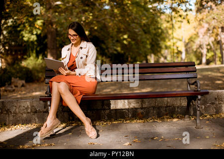 Femme assis sur un banc dans le parc en automne météo à l'aide de tablet pc et contrôler les médias sociaux. Banque D'Images