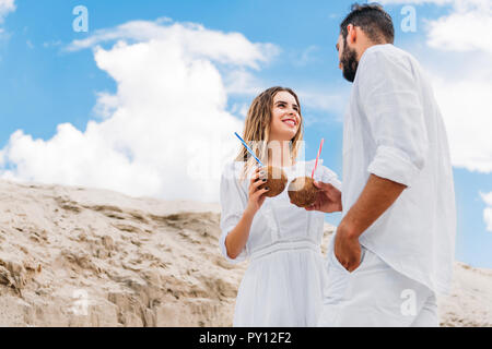 Vue de dessous du couple en blanc avec des cocktails à la noix de coco en face de ciel bleu Banque D'Images