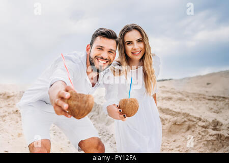 Happy young couple en blanc avec des cocktails de coco looking at camera Banque D'Images