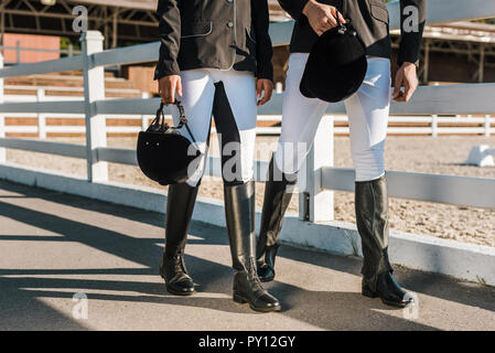 Image recadrée de cavaliers en vêtements professionnels autour de clôture et la tenue des casques d'équitation au Ranch Banque D'Images