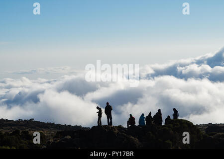 Silhouette de groupe de guides et porteurs en faisant une pause très haut au-dessus des nuages sur le mont Kilimandjaro avec ciel bleu en arrière-plan Banque D'Images