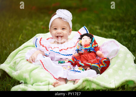 Happy smiling girl with doll siéger sur fond d'herbe verte Banque D'Images