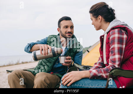 Couple drinking thé chaud au cours de camping Banque D'Images