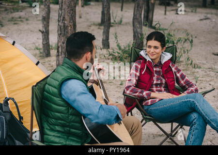 Homme jouant de la guitare acoustique de smiling épouse sur camping Banque D'Images