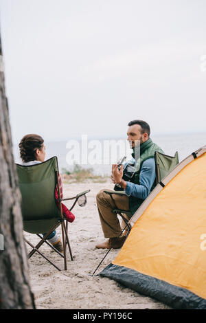 Homme jouant de la guitare acoustique pour femme sur le camping Banque D'Images