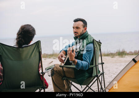 Homme jouant de la guitare acoustique pour femme sur le camping Banque D'Images