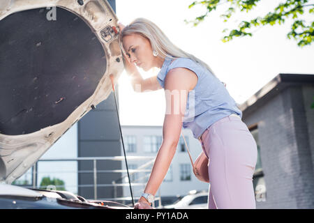 Vue de côté pensive woman sous un capot de voiture de voiture cassée sur street Banque D'Images