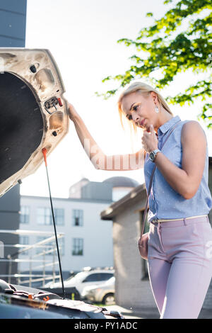 Vue de côté pensive woman sous un capot de voiture de voiture cassée sur street Banque D'Images