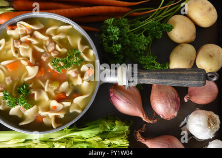 Un pot de soupe poulet et nouilles fraîches maison entouré par certains des ingrédients. Banque D'Images