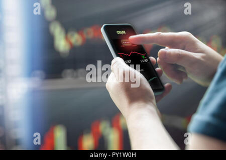 Mans hand holding mobile phone contre the stock market charts Banque D'Images