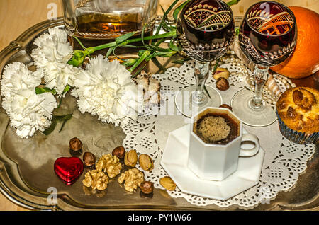 Du café noir et des oeillets,vieux verres cristal avec une bouteille de liqueur, écrous et une orange, de perle, de coquillages sur un plateau d'argent nickel Banque D'Images