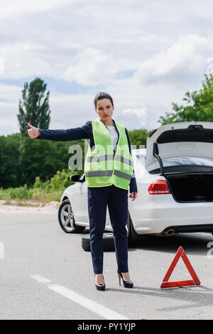 Attractive businesswoman en vert clair sont acquises sur l'auto-stop près de la route voiture cassée Banque D'Images