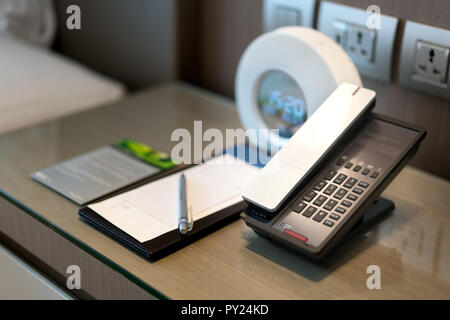 Téléphone noir et remarque à l'avant et lit dans l'arrière-plan, l'accent sur le téléphone,pour le service en chambre,thèmes de communication dans l'hôtel ou resort. Banque D'Images