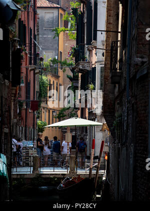 Une vue vers le bas d'un canal à la recherche vers les touristes traversant un pont un jour d'été à Venise. Banque D'Images