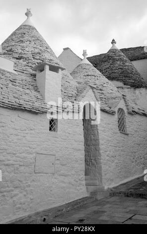 Au toit conique blanchis à la maison derrière trulli mur blanc dans la ville de Alberobello dans les Pouilles, Italie du Sud. Photographié en monochrome. Banque D'Images