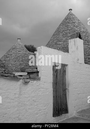 Au toit conique blanchis à la maison derrière trulli mur blanc dans la ville de Alberobello dans les Pouilles, Italie du Sud. Photographié en monochrome. Banque D'Images