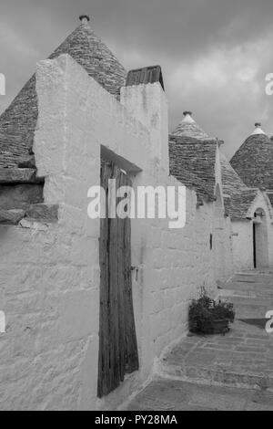 Au toit conique blanchis à la maison derrière trulli mur blanc dans la ville de Alberobello dans les Pouilles, Italie du Sud. Photographié en monochrome. Banque D'Images