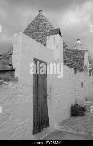 Au toit conique blanchis à la maison derrière trulli mur blanc dans la ville de Alberobello dans les Pouilles, Italie du Sud. Photographié en monochrome. Banque D'Images