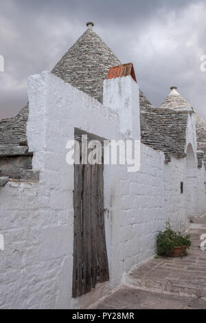 Alberobello, Italie. Au toit conique blanchis à la maison wahsed trulli derrière un mur blanc, dans la ville de Alberobello dans les Pouilles, Italie du Sud Banque D'Images