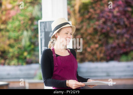 Portrait of a smiling waitress dans un restaurant en plein air holding spéciaux Banque D'Images