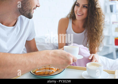 Cropped shot of smiling young couple having croissants et café pour le petit déjeuner au lit Banque D'Images