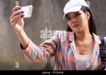 Belle femme asiatique en tenant à l'aide de téléphone mobile à l'extérieur selfies Banque D'Images