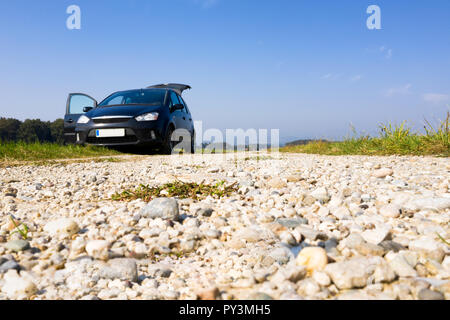 Van noir stationné sur la route de gravier, low angle, copyspace, tronc et porte ouverte, personne, le tout-terrain, le camping dans la nature, le ciel bleu en arrière-plan Banque D'Images