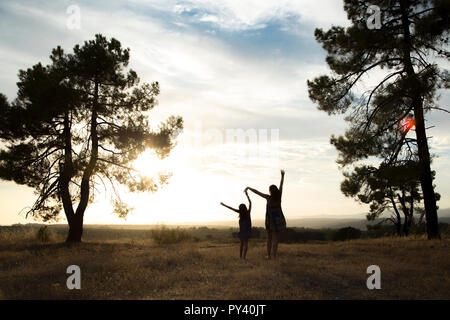 Contre-jour d'une mère et d'une fille dans une forêt de pins avec ciel jaune Banque D'Images