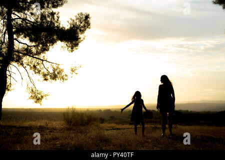 Contre-jour d'une mère et d'une fille dans une forêt de pins avec ciel jaune Banque D'Images