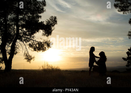 Contre-jour d'une mère et d'une fille dans une forêt de pins avec ciel jaune Banque D'Images