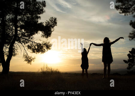 Contre-jour d'une mère et d'une fille dans une forêt de pins avec ciel jaune Banque D'Images