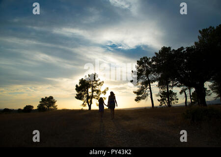 Contre-jour d'une mère et d'une fille dans une forêt de pins avec ciel jaune Banque D'Images