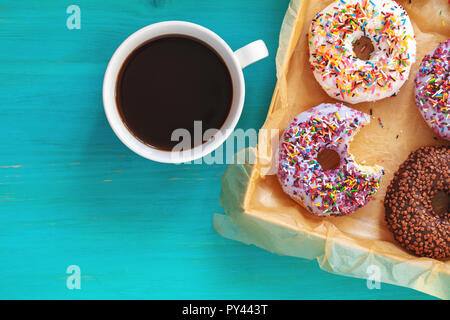 De délicieux beignets glacés à la case et tasse de café sur la surface bleu turquoise. Mise à plat des aliments minimaliste art fond. Vue d'en haut. Banque D'Images