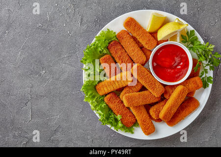 Vue supérieure de l'crumbed les bâtonnets de poisson servi sur une plaque blanche avec du citron, des feuilles de laitue et de la sauce tomate, vue de dessus, télévision lay, close-up Banque D'Images