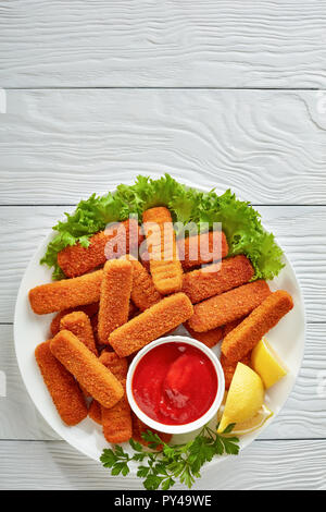 Vue supérieure de l'crumbed les bâtonnets de poisson servi avec du citron, des feuilles de laitue et de la sauce tomate sur une assiette blanche sur une table wooen, vue horizontale à partir de ci-dessus, Banque D'Images