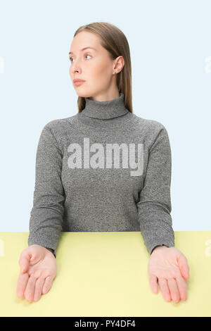 Entreprise sérieuse woman sitting at table bleu sur fond de studio. Le portrait dans le style minimaliste Banque D'Images