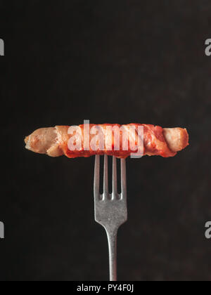 Prêt-à-manger saucisses porc enrobé de bacon sur fourche rustique. Saucisses frites salé enrobé de bacon isolé sur fond noir. L'espace de copie pour le texte. Banque D'Images