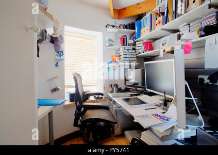 La prise d'un bureau malpropre dans un bureau à domicile, la chambre est petite et encombrée, sur le bureau est de trois écrans d'ordinateurs et de fournitures de bureau. Banque D'Images