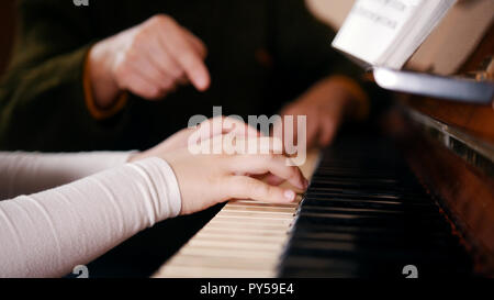 Un ancien enseignant qui petite fille comment jouer au piano. Mains Banque D'Images